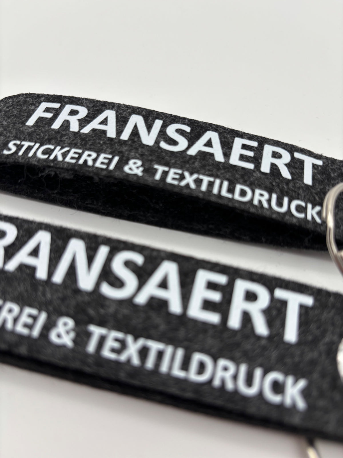 Filz-Schlüsselanhänger aus grauem Filz mit weißem Fransaert-Logo als Muster